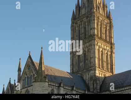 Salisbury Cathedral in late afternoon winter sunshine. A half moon hangs in the blue sky above. Stock Photo