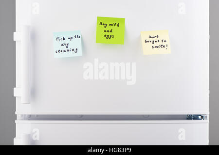 Pick up the dry cleaning, buy milk and eggs, dont forget to smile notes on blue, green and yellow sticky paper on white refrigerator door Stock Photo