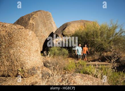 Happy couple walking on dirt road by rock foramtions against clear blue sky Stock Photo