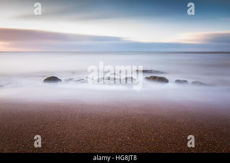 Rocks on the beach being submerged by the incoming tide during sunset Stock Photo