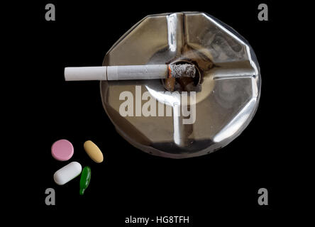 Lighted cigarette on an ashtray alongside medicine pills - Public awareness message "Smoking is injurious to health". Stock Photo