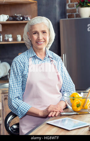 Senior woman in apron smiling at camera in kitchen Stock Photo