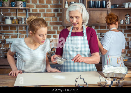 Grandmother and granddaughter sifting flour for cookies in kitchen Stock Photo