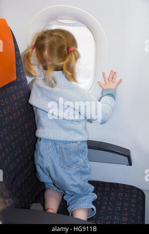 Kid child / toddler / children age 2 on holiday vacation looking looks look out from window seat while flying on air plane / airplane aeroplane flight Stock Photo