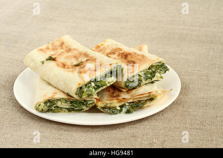 Roasted rolls of bread lavash filled with herbs and feta cheese at white plate on rough linen cloth Stock Photo