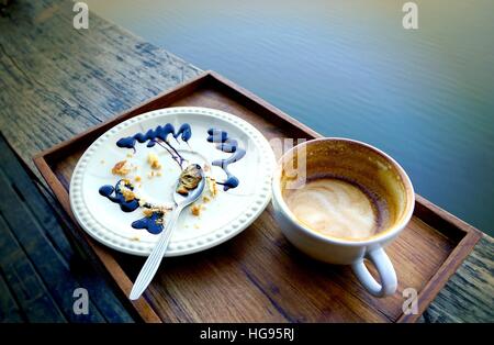 Empty coffee cup and white plate with crumbles of eaten cake and used spoon , dirty after finish breakfast. Stock Photo