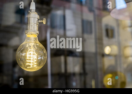Decorative old Edison style light bulb against blurred urban scene reflecting background Stock Photo