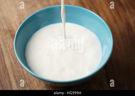 fresh milk poured into blue bowl on wood table Stock Photo