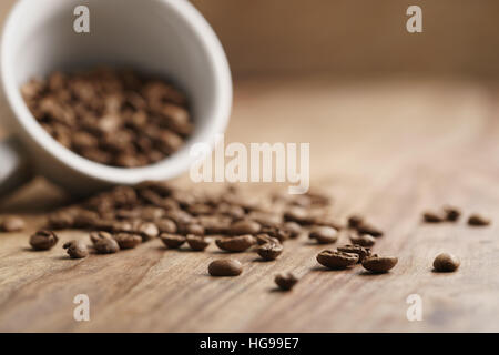 overturned cappuccino cup with roasted coffee beans on wood table Stock Photo