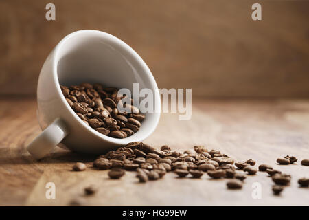 overturned cappuccino cup with roasted coffee beans on wood table Stock Photo