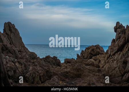 Closeup large formation of rocks on shoreline between beach and sea against blue sky and white clouds Stock Photo
