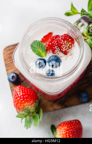 Strawberry smoothie topped with fresh strawberries, blueberries, chia seeds and mint leaf served in glass cup