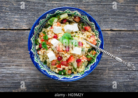 Tabbouleh salad with soft white cheese and pomegranate seeds in bowl on wooden background Stock Photo