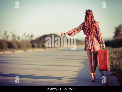 Young hippie woman hitchhiking on the road. Rear view Stock Photo