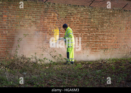 Male council worker using a high pressure water hose to remove graffiti from a brick wall - York, North Yorkshire, England. Stock Photo