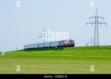 German train driving on Hindenburg Dam towards the island Sylt with green grass and electricity poles, Germany Stock Photo