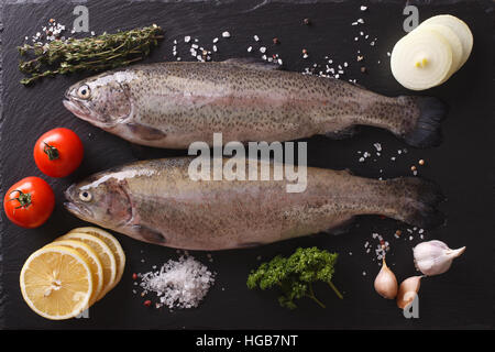 Two raw rainbow trout with ingredients on a slate board closeup. horizontal view from above Stock Photo