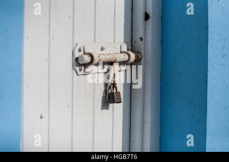 Pad Lock and heavy bolted door. A padlocked white door with a heavy rusting steel bolt holding it secure in a blue painted stucco building. . Hopetown Stock Photo
