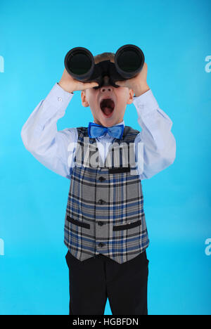 Curious schoolboy looking through binoculars. Photos on a blue background Stock Photo