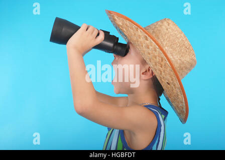 Curious boy in cowboy hat looking through binoculars. Photo on a blue background Stock Photo