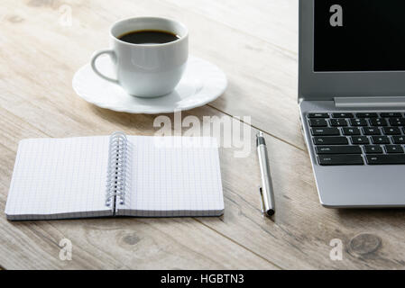 Blank notepad and a pen next to a laptop and coffee on a wooden vintage desk Stock Photo