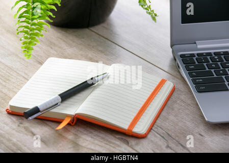 Feminine little notebook on a vintage wooden table next to a laptop and flower Stock Photo