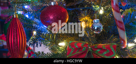 Christmas tree decorations.  Glowing red christmas holiday tree ornaments hanging from branches on a small faux indoor tree. Stock Photo