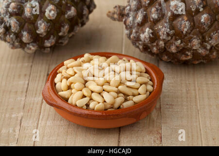Bowl with pine nuts with fresh pinoli, pine cones in the background Stock Photo