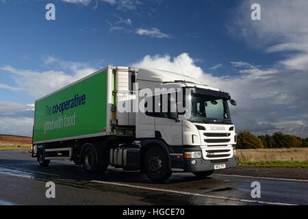 Scania truck towing refrigerated Co-Operative Food trailer on a wet road in Derbyshire with moorland behind and a cloudy sky abo Stock Photo