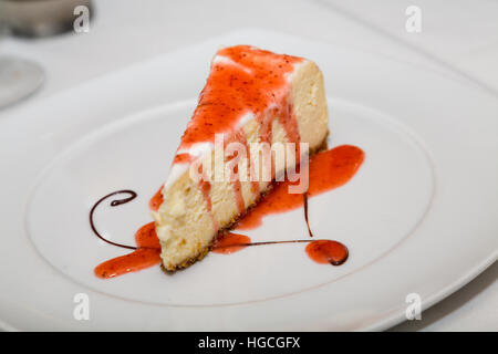 Slice of Cheesecake with Strawberry Sauce and Chocolate Swirl Swirl on White Plate Stock Photo