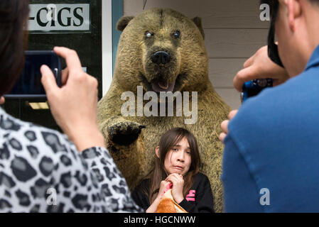 Shops in Downtown. Fear. Asian tourists photographing her daughter next to a stuffed bear. S Franklin street. Alaska Shirt Company. Alaska, USA.  The Stock Photo