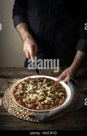 Man cuts the finished pizza on a white dish vertical Stock Photo