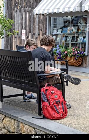 Two boys sitting on an sidewalk bench doing homework with their backs to the camera Stock Photo