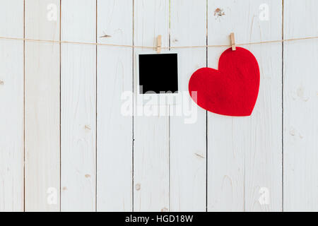 Red heart and photo frame blank hanging at clothesline on wood white background with space. Valentine Day.