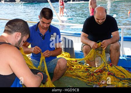 Three Cretan fishermen tending to their fishing nets on a small fishing boat in the harbour, Bali, Crete, Greece, Europe. Stock Photo