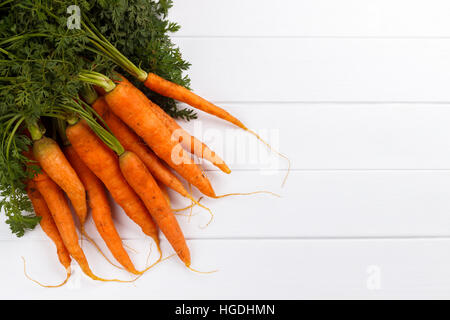 bunch of freshly harvested carrots with soil on white wooden background Stock Photo