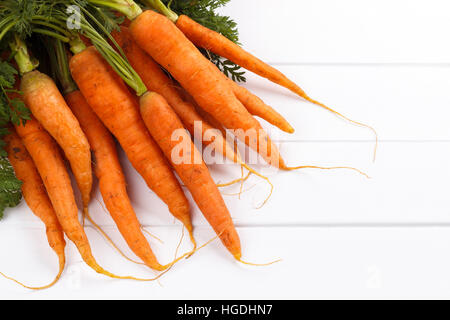 bunch of freshly harvested carrots with soil on white wooden background Stock Photo