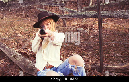 Young woman by a fence pointing gun at the camera Stock Photo