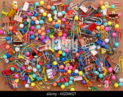 Stationery on cork background - colorful paper clips, rubber bands, push pins, treasury tags and binder clips Stock Photo