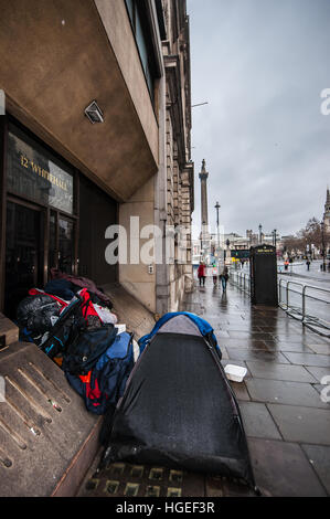 A homeless person camping in Whitehall, with Trafalgar Square and Nelson's Column beyond. Wet from rain Stock Photo