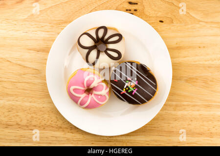 Doughnuts with icing in a white plate on wooden board Stock Photo