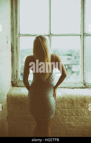 Rear view of a blond woman standing by the window Stock Photo