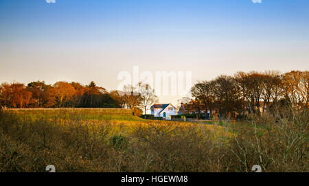 Autumnal landscape of picturesque English cottage amongst trees and under blue skies and autumnal coloured foliage Stock Photo