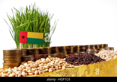 Guinea Bissau flag waving with stack of money coins and piles of wheat and rice seeds Stock Photo