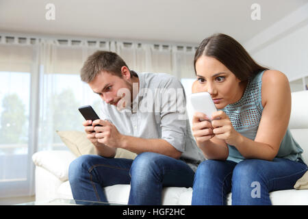 Obsessed couple of roommates with their smart phones ignoring each other sitting on a couch at home Stock Photo