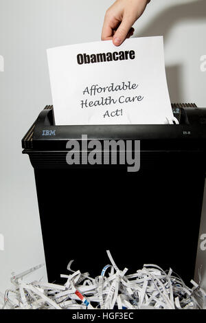 Obamacare headed text paper with affordable health care act below being fed into a paper shredder Stock Photo