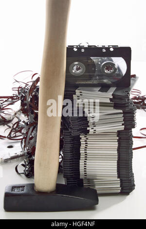 Hammer in front of a stack of floppy disks and an audio tape, jammed cassette tape in background Stock Photo