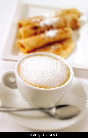 Cup of cappuccino, blurred crepes in background Stock Photo