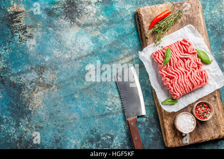 Raw minced meat with olive oil and seasoning on paper over blue stone background. top view with copy space. Stock Photo
