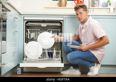 Bored Man Loading Dishwasher In Kitchen Stock Photo